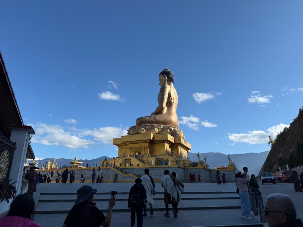 Seitenansicht der 51 Meter hohen, vergoldeten Buddha Dordenma Statue in Thimphu, die majestätisch über dem Tal thront, umgeben von Pilgern.