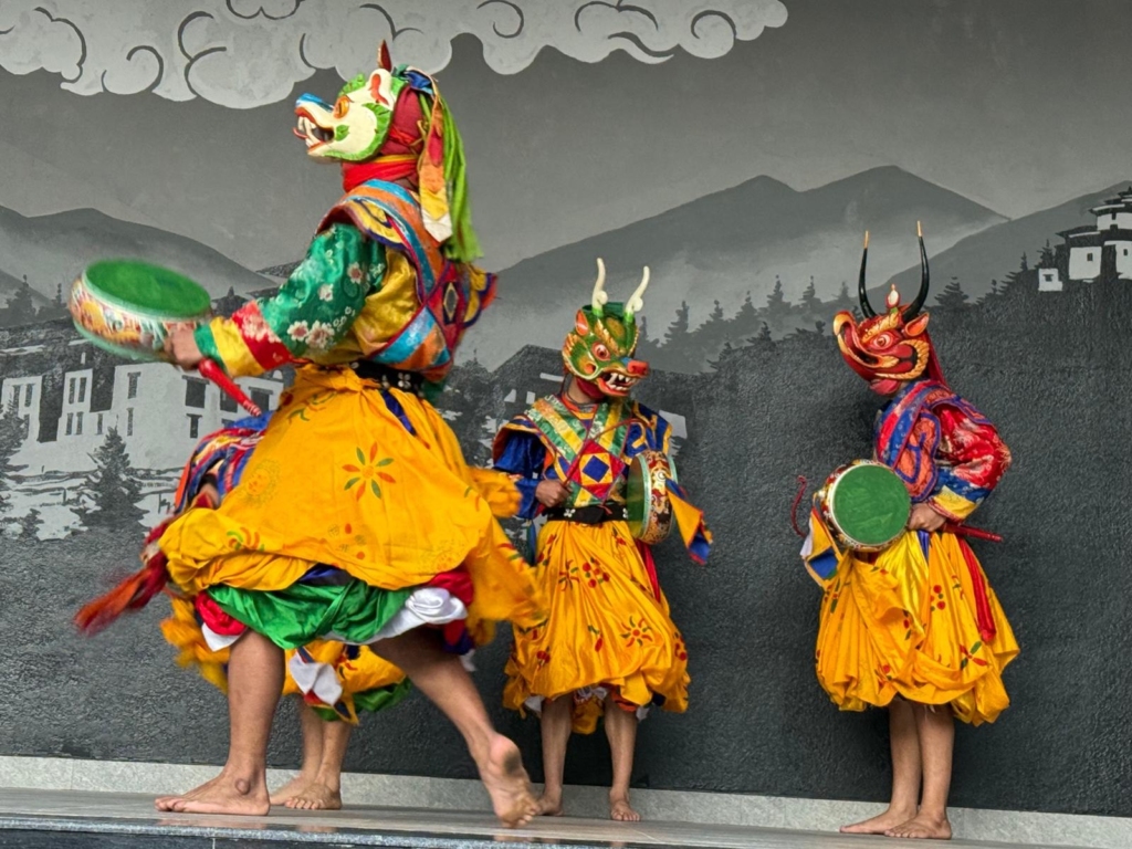 Traditional mask dancers (Cham) in colorful costumes holding hand drums performing a dynamic ritual dance on stage.
