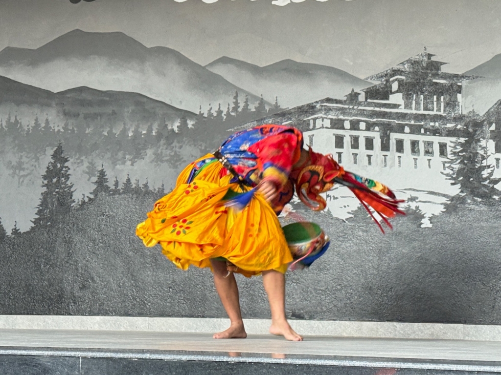 A solo mask dancer (Cham) wearing a bright yellow skirt demonstrating a deep, sweeping movement during the cultural performance.
