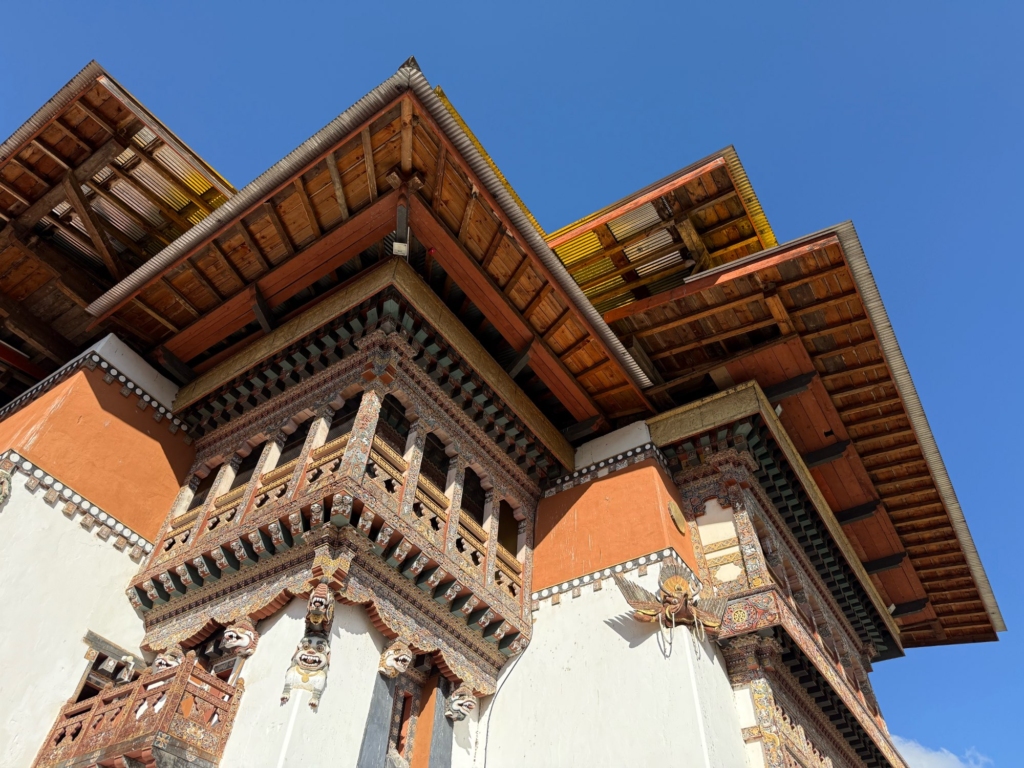 Low-angle view of the elaborate roof construction of Gangtey Monastery, showcasing intricately painted wooden beams and golden corner decorations.