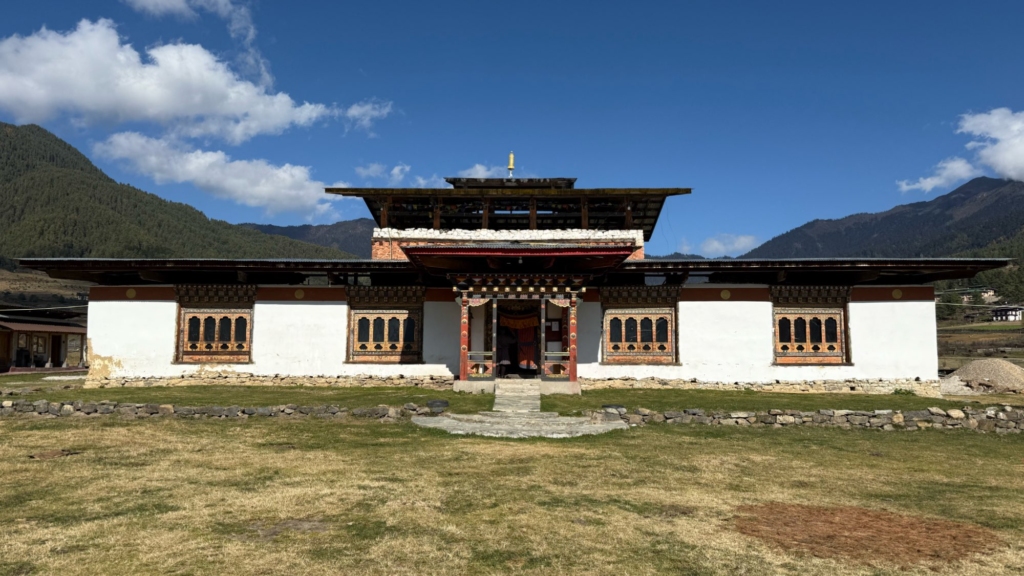 Front view of the historic Khewang Lhakhang temple in the Phobjikha Valley featuring traditional windows and a white facade situated on a meadow.