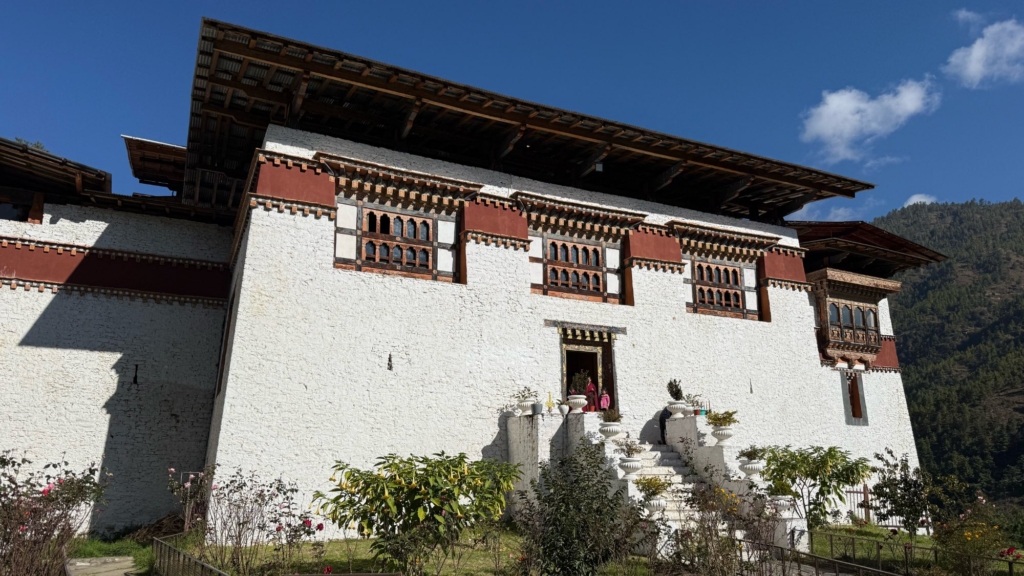 The massive white walls and typical Bhutanese fortress architecture of the Semthoka Dzong under a bright blue sky.