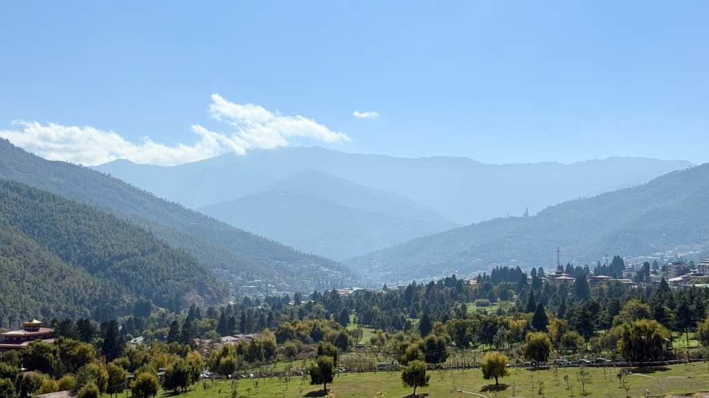 Scenic panoramic view over the green Thimphu Valley, with the distinctive Buddha Dordenma statue visible in the distance atop the mountain.